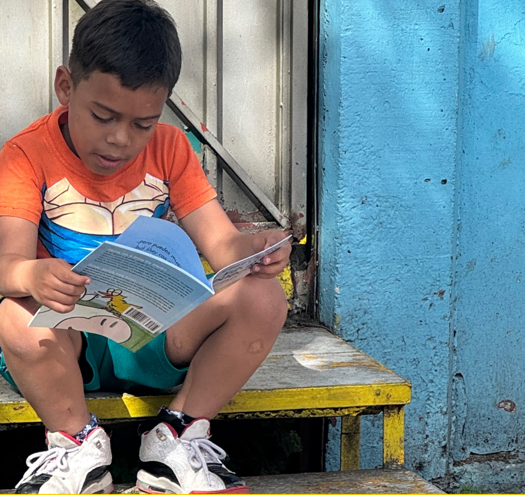A boy reading a bilingual book on a porch step