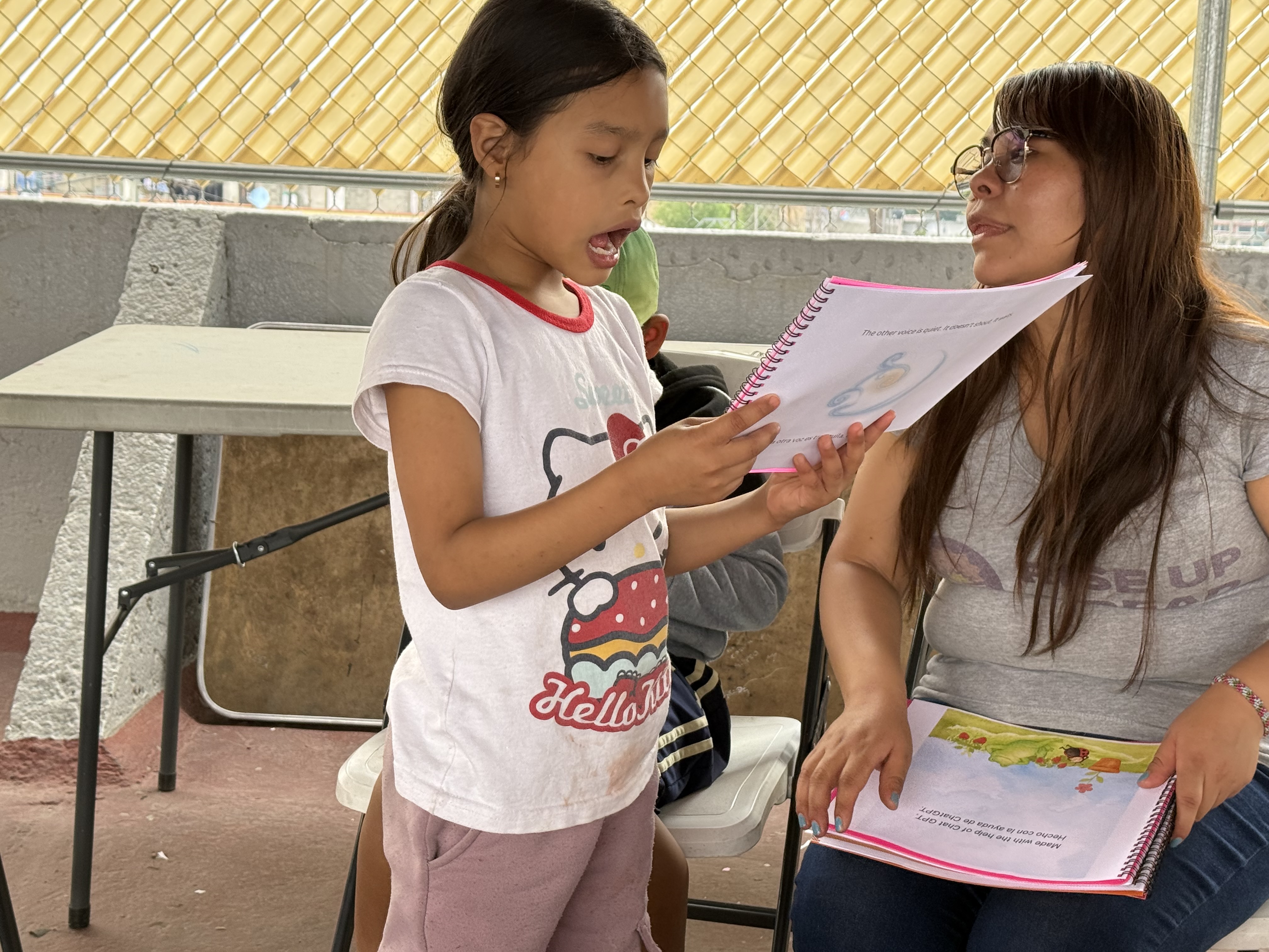 A girl reading a bilingual book aloud with a volunteer