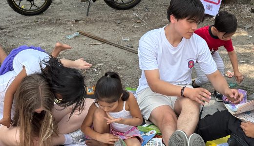 A student volunteer reading and colouring with young children at Camp Mysterio